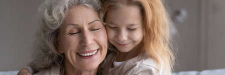 Happy faces of excited older grandmother and little preteen girl granddaughter cuddling after long...