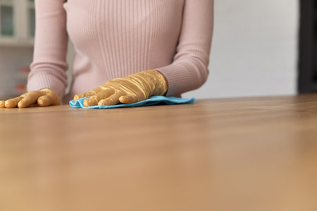 Close up young woman tidy housewife wearing yellow rubber gloves, cleaning wooden table or countertop in modern kitchen. Professional female cleaning service worker wiping furniture, mopping dust.の写真素材