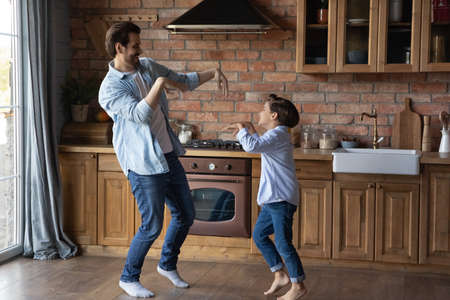 Happy dad teaching excited cute preschooler son to dance. Daddy and kid having fun, listening to music, exercising together, enjoying leisure and home activity. Active family, fatherhood conceptの写真素材