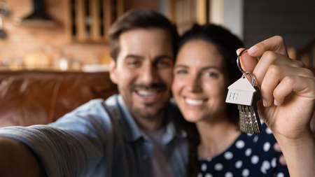 Happy young husband and wife showing key at camera, taking selfie. Property buyers, tenants celebrating mortgage approval, rent apartment, buying first house. New home, real estate conceptの写真素材