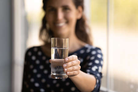 Happy woman showing glass of fresh pure natural water, toasting at camera, holding transparent glass, smiling in background, keeping healthy habit, diet and detox, hydration balance. Close up of handの写真素材