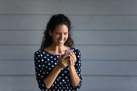 Joyful excited cellphone user reading on digital screen and laughing out loud. Happy woman using virtual app, online service for texting, chatting checking messages, email, looking at display, smilingの写真素材