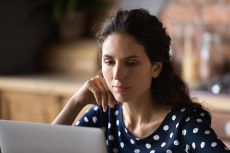 Focused adult student woman using laptop in kitchen, working or studying from home, watching learning webinar, reading ebook or email, making video call, browsing internet, social media, shoppingの写真素材