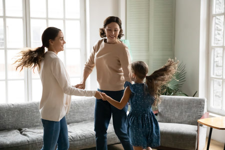 Overjoyed three generations of Caucasian women have fun dance together on family weekend at home. Smiling little girl with mother and grandmother relax rest in living room celebrate relocation.の写真素材