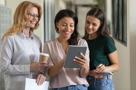 Mixed race leader showing virtual presentation on tablet to employees. Happy diverse female business group of different ages using and sharing digital device, making online video call togetherの写真素材