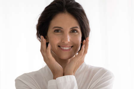 Headshot portrait of happy millennial latin female in white gown smiling caressing cheeks with shiny...
