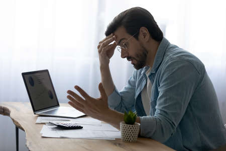 Stressed anxious young man feeling frustrated of made mistakes in financial payments, feeling lack of money calculating domestic expenses, paying bills or taxes online, bank debt bankruptcy concept.の写真素材