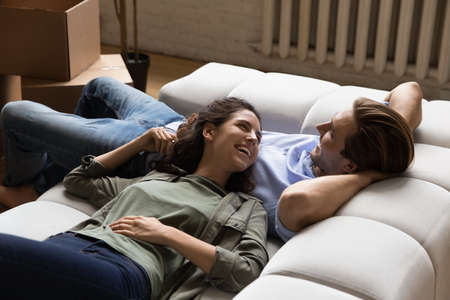 Imagining new life. Serene married couple relax on comfy sofa talk discuss relocation planning decor of new flat. Loving spouses rest on sofa at modern house after unpacking belongings at moving dayの写真素材