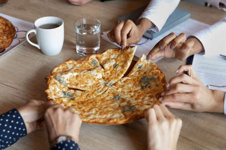 Hot pizza on office table, hands of employees taking slices. Team of company workers ordering fast food delivery for lunch during meeting or party, eating takeaway unhealthy meal, junk food. Close upの写真素材