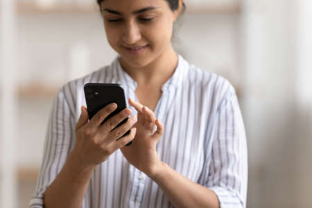 Close up cropped of Indian woman using phone, typing on screen, writing message in social networks, young female browsing mobile device apps, shopping or chatting online, holding smartphoneの写真素材