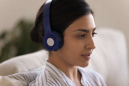 Close up side view of confident Indian woman in modern wireless headphones speaking, serious young female speaking, involved in internet meeting, conference, chatting online, making video callの写真素材