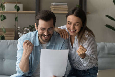 Beautiful couple read letter notification news from bank feel overjoyed clench fists make yes gesture, succeed goal, celebrate incredible offer received, loan approval looking happy. Success conceptの写真素材