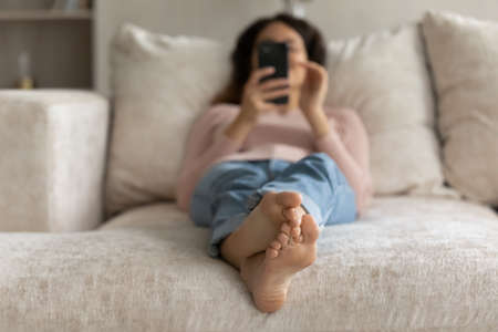 Close up crop focus view of young Latino woman relax on sofa at home using cellphone gadget. Happy...