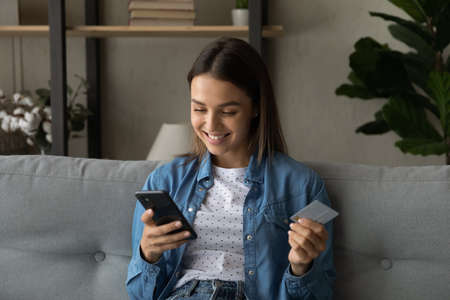 Happy young woman buy on internet holding credit card use smartphone retail services and virtual...