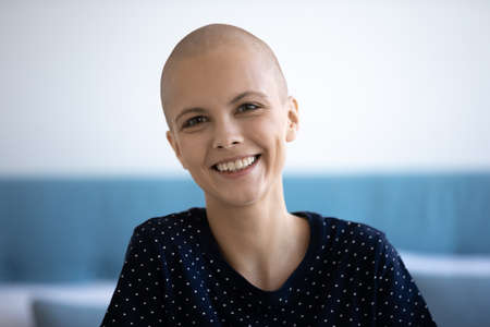 Head shot portrait of smiling young sincere hairless after chemotherapy woman, feeling optimistic in cancer fight. Joyful laughing candid millennial bald lady with inner strength looking at camera.の写真素材