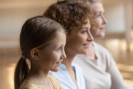Head shot profile portrait of smiling three generations of women looking to aside visualizing good...