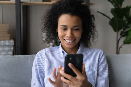 Smiling African American woman look at smartphone screen have webcam digital virtual event online. Happy biracial female speak talk on video call on cellphone. Communication, technology concept.の写真素材