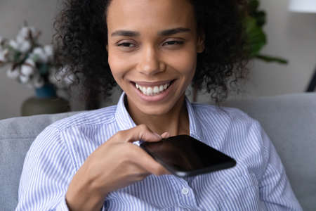 Close up of smiling young African American woman use cellphone activate digital voice assistant on gadget. Happy biracial female record audio message on smartphone, talk speak on call on loudspeaker.の写真素材