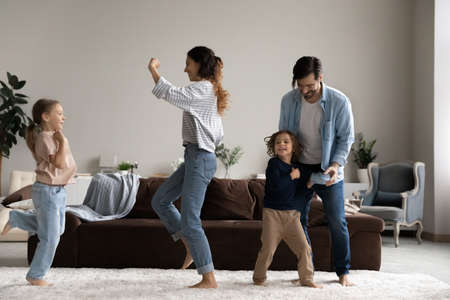 Excited happy family dancing to music in living room, having fun together, enjoying home party, activities and exercises. Couple of parents and funny energetic kids celebrating new house buyingの写真素材