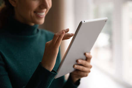 Cropped close up smiling woman typing on tablet screen, writing message in social network, chatting,...