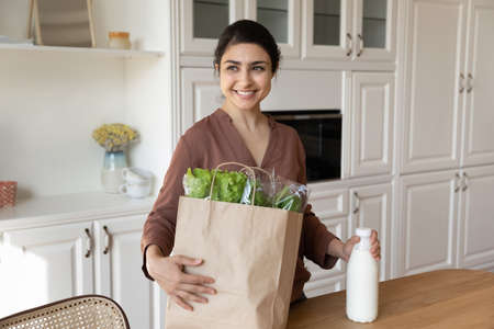 Happy millennial Indian woman shopping for healthy vegetarian organic or bio products. Smiling young ethnic female unbox package bag buy farmer goods at supermarket. Online delivery, diet concept.の写真素材