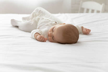 Cute little newborn son or daughter lying on white sheets in cozy bedroom at home take nap daydream....