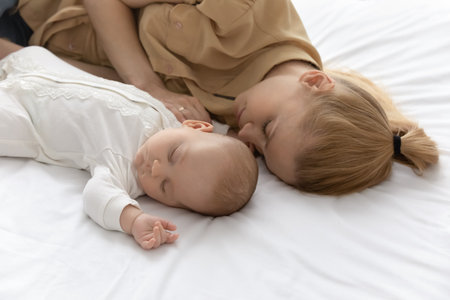 Young Caucasian mother and little baby infant kid child lying sleeping together in cozy white bed at...