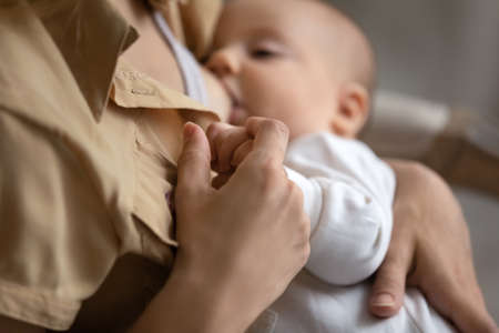 Crop close up of loving young Caucasian mother hug lull little newborn child breastfeed at home. Caring mom caress comfort put to bed small baby infant kid, feed with breast milk. Motherhood concept.の写真素材