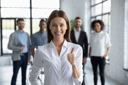 Portrait of smiling young Caucasian businesswoman stand forefront show thumb up give recommendation. Happy female employee or client recommend good quality company service. Review concept.の写真素材