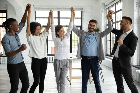Overjoyed diverse multiethnic businesspeople raise hands up celebrate shared business success or...