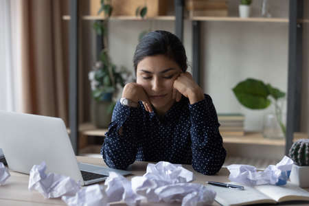 Exhausted millennial Indian woman sit at desk at home office fall asleep try to meet deadline. Tired...