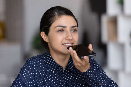 Young Indian female client or customer use cellphone device record audio message. Millennial...