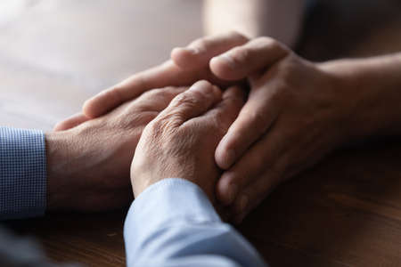 Crop close up of old Caucasian father and adult son hold hands show family unity and support. Supportive mature dad and grownup child demonstrate love care, comfort and caress. Bonding concept.の写真素材