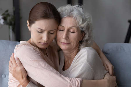 Caring millennial woman child embrace unhappy upset old 60s mother show love and care. Supportive adult grownup daughter hug sad mature mom comfort and caress parent. Family support concept.の写真素材