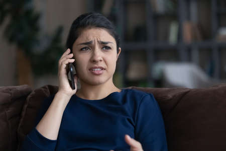 Unhappy young Indian woman feel distressed hear bad news talking speaking on smartphone. Upset confused mixed race female frustrated depressed get negative message on cellphone call.の写真素材