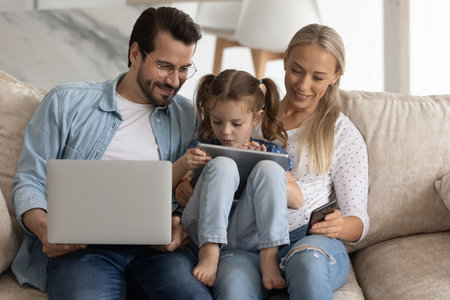 Happy family couple with little kid engaged in gadgets using, resting on sofa at home together....