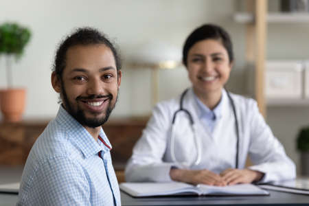 Smiling millennial healthy african american multiracial patient satisfied with visiting indian female doctor, looking at camera in modern clinic office room, medical insurance healthcare concept.の写真素材