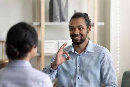 Smiling young handsome african american man using sign language, practicing communication with...