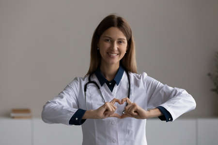 Portrait of happy sincere kind woman doctor general practitioner physician pediatrician medical worker in white coat showing heart love symbol, expressing support to patients, donation, healthcare.の写真素材