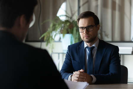 Confident man wearing glasses and suit candidate waiting for hr manager decision at meeting, job interview concept, hiring process, recruiter employer reading resume cv, considering applicationの写真素材