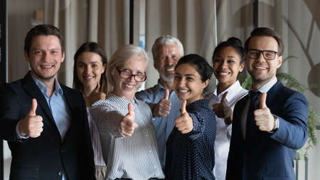 Happy successful diverse businesspeople employees group showing thumbs up together, looking at camera, standing in office, excited colleagues team recommending best corporate service, good careerの写真素材