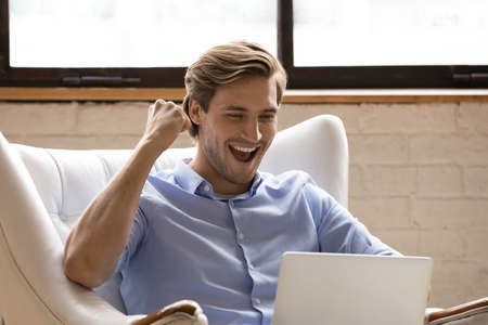Overjoyed millennial handsome man looking at computer screen, feeling excited of reading email with...