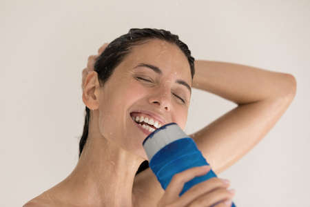 Head shot bare happy millennial hispanic latina woman singing song using plastic shampoo gel bottle...