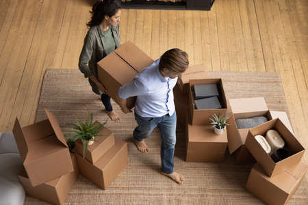 Above top view happy young barefoot family couple homeowners carrying big box with stuff into renovated stylish living room, involved in moving own belongings in new apartment, relocation concept.の写真素材