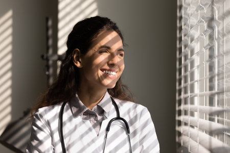 Happy satisfied medical professional looking out of window at morning sun, thinking of patients rehabilitation, future vision, career of doctor, feeling joy about promotion, Head shot portraitの写真素材