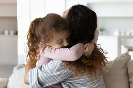 Loving small child girl cuddling affectionate mother after long separation time, showing tender sweet feelings at home. Happy two female generations family embracing, warm relations concept.の写真素材