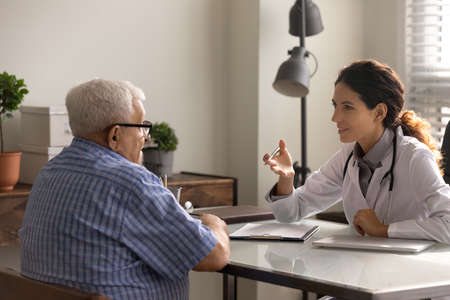 Elder male patient visiting doctor in office in hospital, consulting practitioner about treatment, complaining of geriatric health problem. Female physician giving advice to senior man at appointmentの写真素材