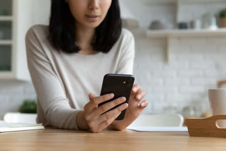 Close up cropped vietnamese asian woman using cellphone, web surfing information, shopping in internet store, typing message communicating in social network, modern technology addiction concept.の写真素材