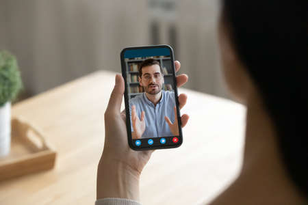 Back shoulder close up view young woman holding mobile web camera video call conversation with male...