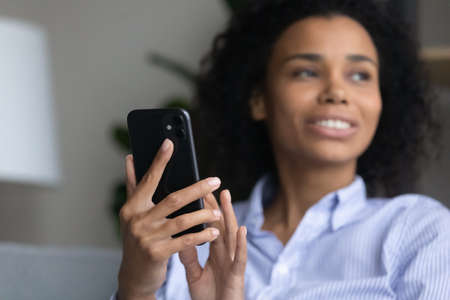 Convenient technology. Blurred shot of millennial biracial woman smartphone user looking aside distracted from device screen. Soft focus on new modern mobile phone gadget in young black female handsの写真素材